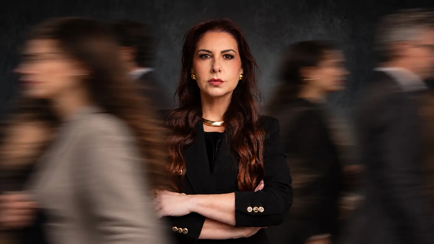 Lidiane Feijó de braços cruzados, de preto, com pessoas em movimento ao redor